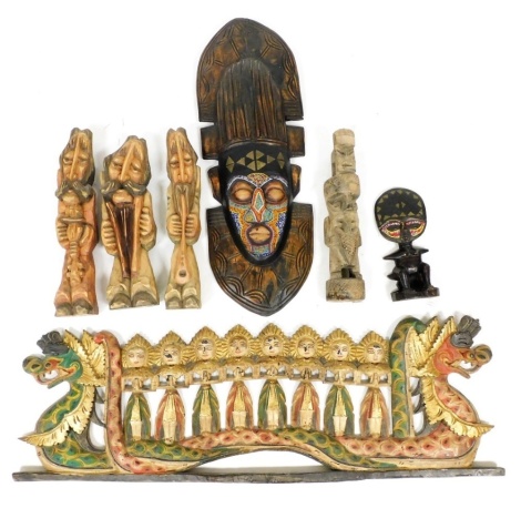 An ethnographic tribal hardwood and bead work mask, 66cm high, a wooden and bead work fertility figure, 24.5cm high, a far Eastern carving of figures on a dragon boat, and four further carved figures. (7)