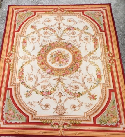 An Aubusson style wall hanging, decorated with a central floral framed basket of roses, against a cream ground of roses garlands and foliate scrolls, 350cm x 276cm.