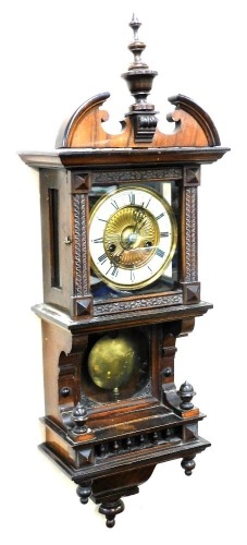 A late 19thC Continental walnut cased drop dial wall clock, the circular brass dial with enamel chapter ring bearing Roman numerals, eight day movement with coil strike, the case with broken arch pediment, with pendulum and key, 78cm high.