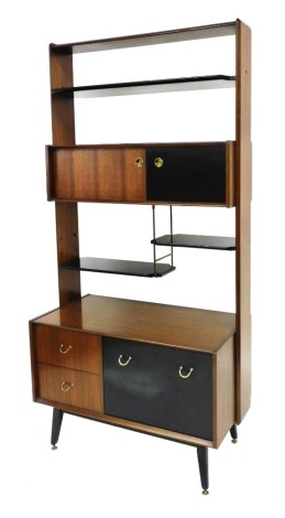 A G-Plan 1950's teak and ebonised lounge unit, the other superstructure with two shelves above a cupboard with two sliding doors, the base with a drop down flap flanked to the left by two drawers raised on turned legs on brass feet, 193cm high, 95cm wide,