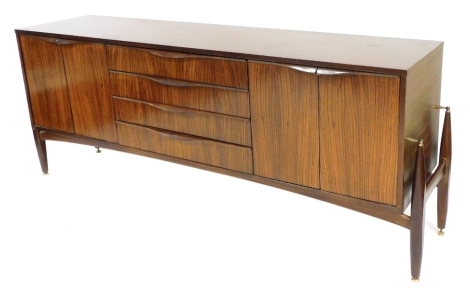 A mid century Elliotts of Newbury teak sideboard, with four long central drawers, flanked by two pairs of cupboard doors, raised on extended turned legs, brass capped, 77cm high, 185.5cm wide, 45cm deep.