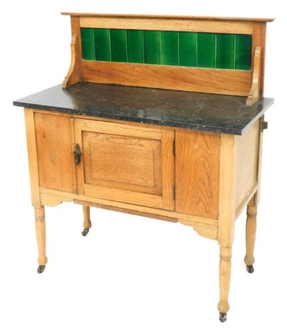 A Victorian oak washstand, with a green tiled splash back, black marble top over a single cupboard door, raised on turned legs, on castors, 106cm high, 92cm wide, 43cm deep.