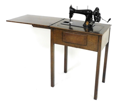 An oak sewing table, the hinged lid opening to reveal an interior with a Singer sewing machine, number S571190, raised on tapering square legs, 79cm high, 61cm wide, 43cm deep.