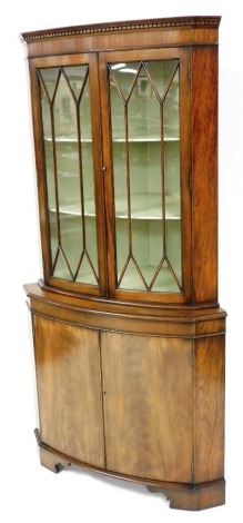 A reproduction mahogany corner cabinet, the dentil moulded pediment over a pair of astragal glazed doors, enclosing a pale green painted interior with two shelves, above a pair of cupboard doors, raised on bracket feet, 179cm high, 83cm wide, 51cm deep.