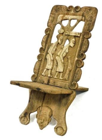 An African carved wood tribal chair, the back carved with two figures and a tree, within a scrolling surround, with solid paddle seat, raised on a front foot carved with a mask and two ball and claw feet, 91cm high.