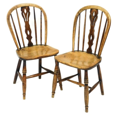 A pair of Victorian oak and elm Windsor kitchen chairs, with pierced vase splat solid saddle seat, raised on turned legs united by an H framed stretcher. 