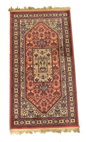 A Persian wool pink ground rug, with central lozenge within multiple floral borders, 159cm x 83cm.