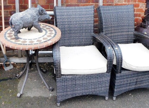 A pair of rattan garden armchairs with removable seats, a mosaic tile top garden table, 73cm high, the top 69cm diameter, and a resin boar garden ornament, 30cm high. The upholstery in this lot does not comply with the 1988 (Fire & Fire Furnishing) Regul