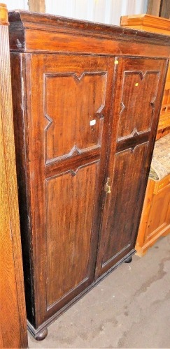 An early 20thC oak double wardrobe, the top with a moulded cornice above two panelled doors, on bun feet, 181cm high, 114cm wide, 52cm deep.