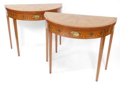 A pair of 19thC Sheraton revival hand painted satinwood demi lune card tables, with baize lined folding tops, oval painted vignettes within painted swags with urns, raised on square taper legs, 77cm high, 46cm deep.