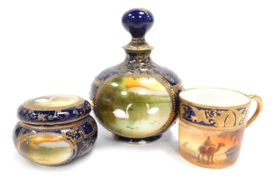 A Noritake trio set, on royal blue ground picked out in gilt, comprising coffee can, vase and cover with swans, 13cm high, and a trinket dish, (AF). (3)