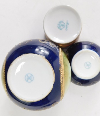 A Noritake trio set, on royal blue ground picked out in gilt, comprising coffee can, vase and cover with swans, 13cm high, and a trinket dish, (AF). (3) - 3