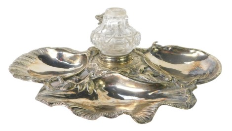 A silver plated 20thC shell capped ink well, the three scallop dishes, with vine detail and applied cut glass ink bottle, with rose bud pen stand, stamped EP, 26cm wide.