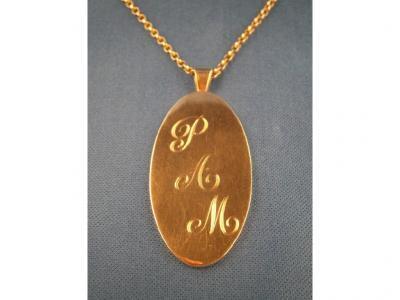 A large oval pendant bearing the initials PAM to one side and a chain