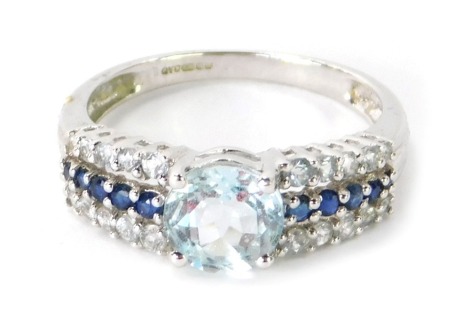 A 9ct white gold dress ring, with central aquamarine on three splayed shoulders set with CZ and sapphire stones, in claw setting, ring size P½, 2.7g all in.