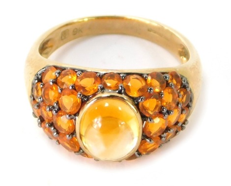 A 9ct gold dress ring, with central cabochon cut citrine, and orange topaz set sides, on darkened should claws, ring size P½, 4.3g.