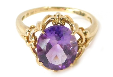 A 9ct gold amethyst dress ring, the oval amethyst in four claw raised setting with outer rococo scroll borders on V splayed shoulders, ring size Q, 4.1g all in.