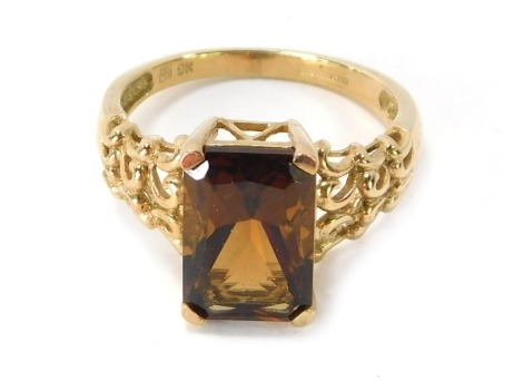 A 9ct gold smoky quartz dress ring, the rectangular cut stone in four claw tension setting, with three layered scroll design on shoulders, ring size P, 3.5g all in.