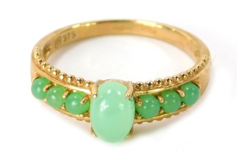 A 9ct gold jade set dress ring, the central raised oval jade in four claw setting with three spherical jade beads to each shoulder, ring size P½, 2.8g all in.