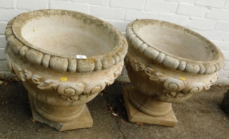 A pair of reconstituted stone planters, each with ribbed and foliate scroll detail, 51cm high, 52cm diameter.