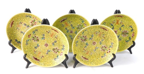 A set of five Chinese small dishes, each on a yellow ground with floral design and plate stands, 15cm diameter.