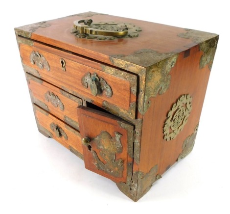 An Eastern hardwood jewellery casket, with brass buckled supports and handle, with one long drawer, cupboard door and two small drawers, 24cm high, 30cm wide, 18cm deep. (AF)