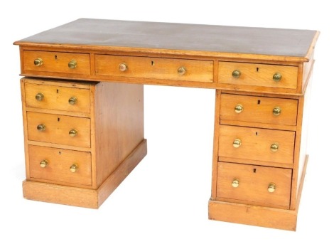 A late 19thC/early 20thC oak pedestal desk, the top with a brown leather inset, above an arrangement of nine drawers, each with brass handles on a plinth, 72cm high, 123cm wide, 68cm deep.