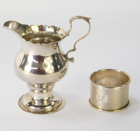 A George III silver cream jug, with fluted top and acanthus leaf handle, on a stepped foot, London 1799, and a George V silver napkin ring, with engine turned decoration bearing the initial F, 3oz. (2)