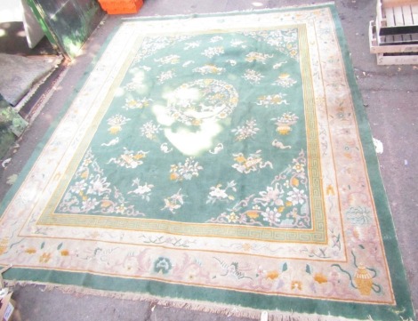 A Chinese carpet, green ground decorated centrally with a circular medallion containing a deer, bird and trees, the ground with bats, flowers and Buddhistic emblems, within a border of birds, butterflies and flowers, 420cm x 344cm.