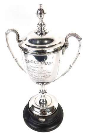 A 1930's Greyhound Racing Club trophy, The Bacci Cup, of campana form with acanthus leaf capped swan neck handles, domed cover with urn finial, on shaped stem and domed circular foot, 47cm high, on a removable ebonised socle, with shield shaped plaque, st