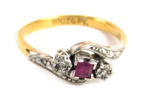 An 18ct cross over dress ring, centred by a ruby, flanked by two illusion set diamonds, with further white stones on a bi-coloured shank, marked 18ct and PT, size L 3.g all in.