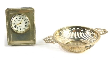 An Elizabeth II silver travel clock, by Kitney & Co London, with 3cm diameter Roman numeric dial, with velvet easel back, London 1996. 7cm high, and a Birmingham two handled strainer dish, with pierced handles. (2)