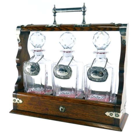 A 20thC oak tantalus, with chrome plated mounts and three cut glass decanters, each with spirit labels, 39cm high.