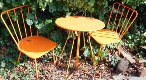 A retro orange metal two seater patio table and chairs, the table with shaped circular top on a bent metal legs, 71cm high, 63cm diameter.