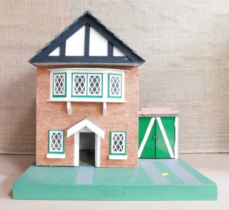 A Tudor style doll's house, twin storey with green and white plastic finish and applied paper brick front, on two tiers with garage, 53cm high, 51cm wide, 36cm deep.