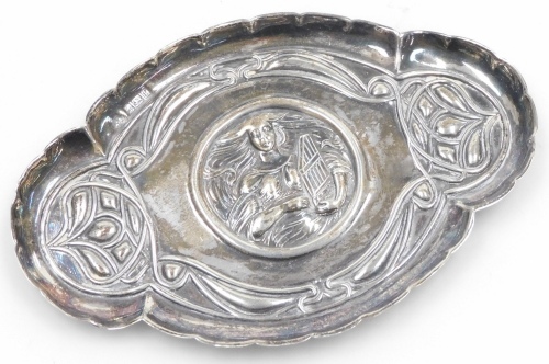 An Edward VII Art Nouveau trinket tray, embossed centrally with a figure of a lady with flowing hair holding a zither, surrounded by typical Art Nouveau motifs, with a raised waved border, William Aitken, Birmingham 1905, 0.97oz, 13.5cm wide.