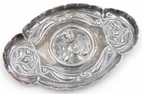 An Edward VII Art Nouveau trinket tray, embossed centrally with a figure of a lady with flowing hair holding a zither, surrounded by typical Art Nouveau motifs, with a raised waved border, William Aitken, Birmingham 1905, 0.97oz, 13.5cm wide.