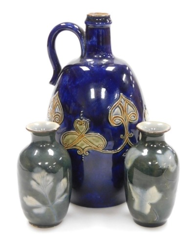 A Royal Doulton stoneware ewer, decorated with applied Art Nouveau motifs against a blue ground, impressed marks, 22.5cm high, and a pair of Royal Doulton Lambeth ware miniature vases, of cylindrical form with flared rims, decorated with ivy leaves in blu