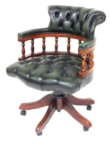 A mahogany and green button leather Captain's chair, with spindle turned supports and X shaped base with castors. The upholstery in this lot does not comply with the 1988 (Fire & Fire Furnishing) Regulations, unless sold to a known exporter or upholstere