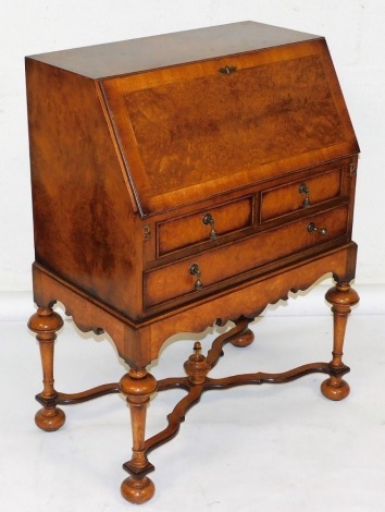 A Georgian style walnut bureau, the feather banded quarter veneered fall enclosing a fitted interior, above two short and one long drawer, each with brass drop handles, on turned supports with flat X shaped stretcher and bun feet, 102cm high, 87cm wide.