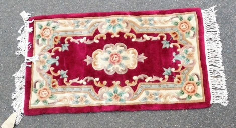 A Chinese wool red ground rug, floral decorated, 117cm x 67cm.