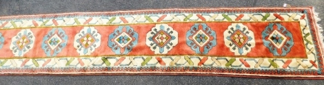 A Turkish wool runner, pink ground with nine medallions within multiple borders, 447cm x 90cm.