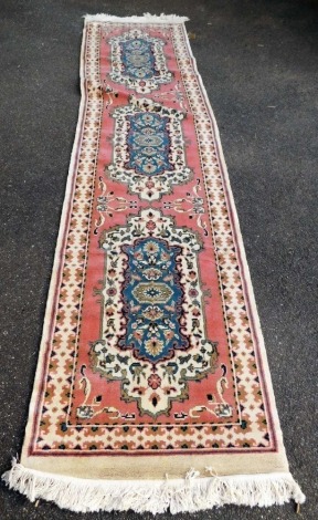 An Eastern wool runner, decorated centrally with three medallions within one wide border, pink ground, 332cm x 85cm.