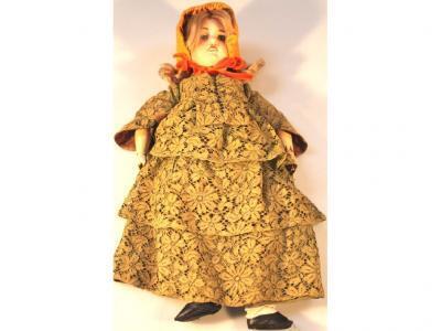 A late 19thC bisque headed doll with composite limbs in green dress petticoats