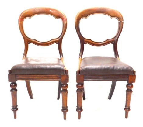 A pair of mahogany balloon back chairs, each with a brown rexine drop in seat, on turned legs.