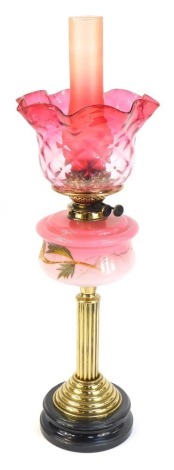 A Victorian cranberry glass oil lamp, with a cranberry glass flared shade and chimney, and a painted floral reservoir on brass column with ebonised base, 71cm high.