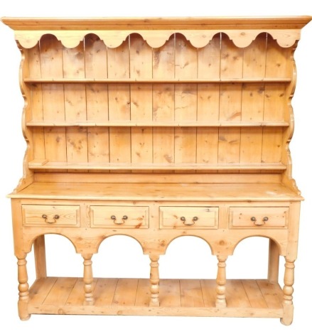 A rustic pine kitchen dresser, top with a moulded cornice and shelves above arrangement of four drawers with arched recesses and a pot board, on bun feet, 189cm high, 177cm wide, 42cm deep.