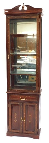 An Eastern hardwood display cabinet, with single glazed door over drawer and cupboard base, with brass inlaid decoration, 209cm high, 56cm wide.