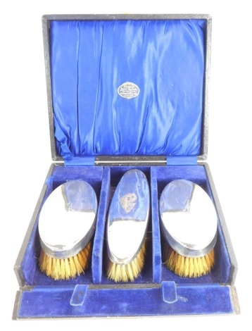 A George V silver dressing table set, bearing the initial J, Birmingham 1918, comprising two short and one long brush in a Baker's Dual Casket Market Place, Wigan presentation box.