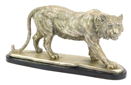 A polished metal model of a prowling tiger, on a mounted black oval base, 24cm high, 49cm, wide, 15cm deep.